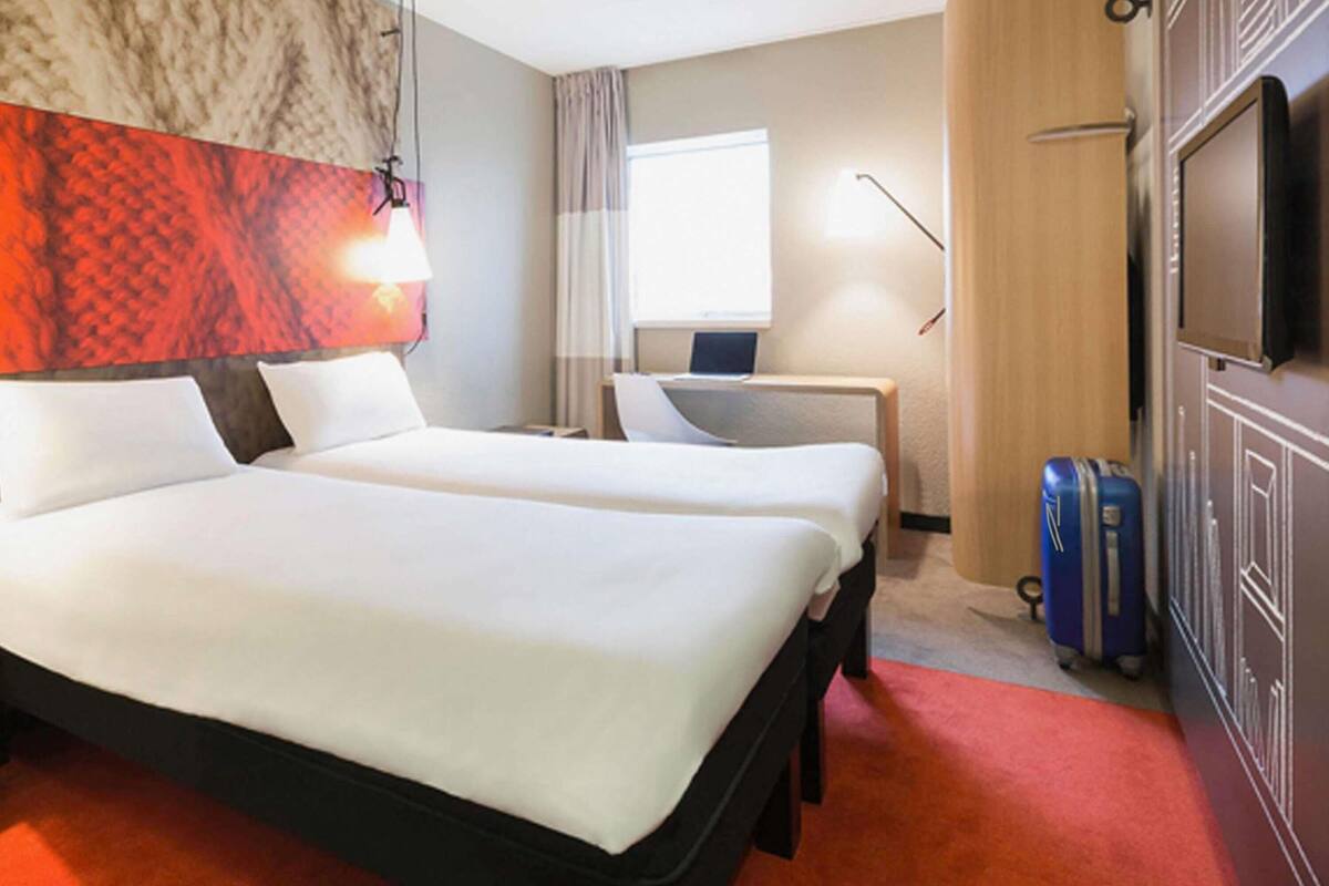 A hotel room with two beds, a desk, a TV, and a suitcase.