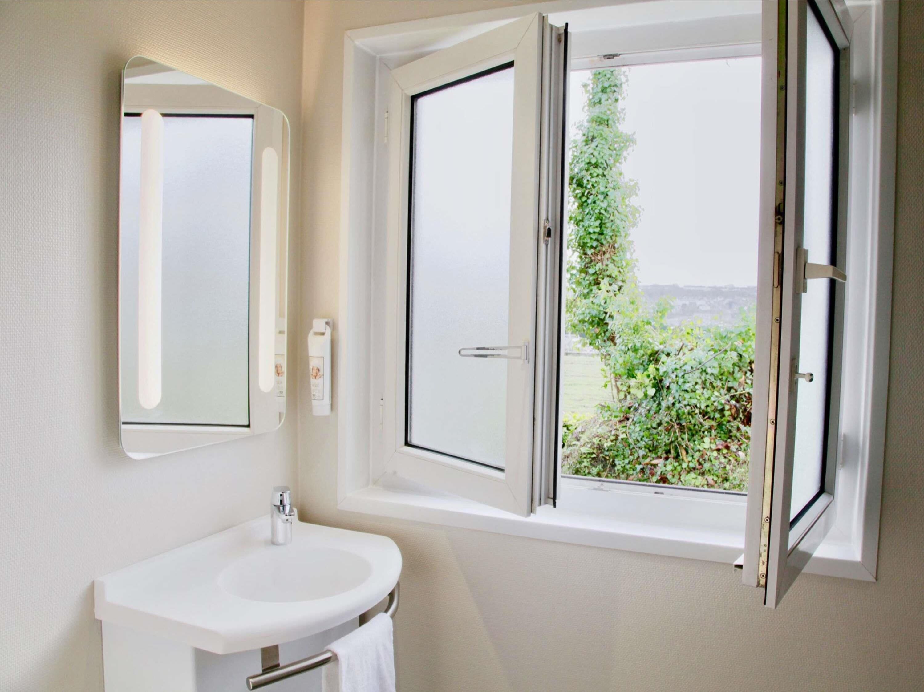Een badkamer met een witte wastafel, een spiegel en een raam met uitzicht op groen.