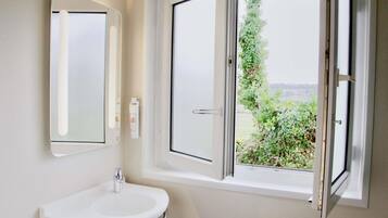 Een badkamer met een witte wastafel, een spiegel en een raam met uitzicht op groen.