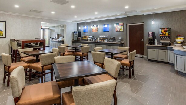 A hotel dining area with multiple tables and chairs, a kitchen area, and a beverage station. - Comfort Inn College Park North (Beltsville)