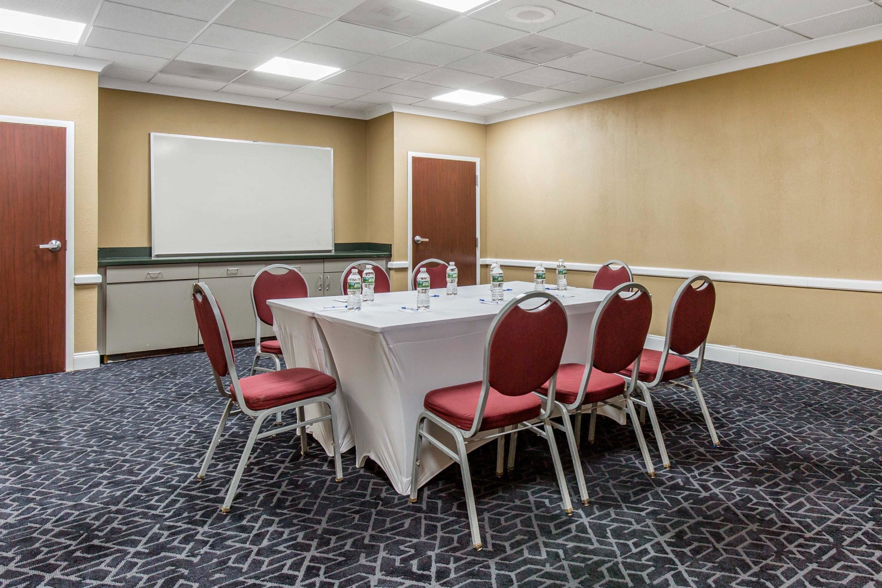 Un salón de conferencias con una amplia mesa, sillas rojas, una pizarra y una pantalla de proyector.
