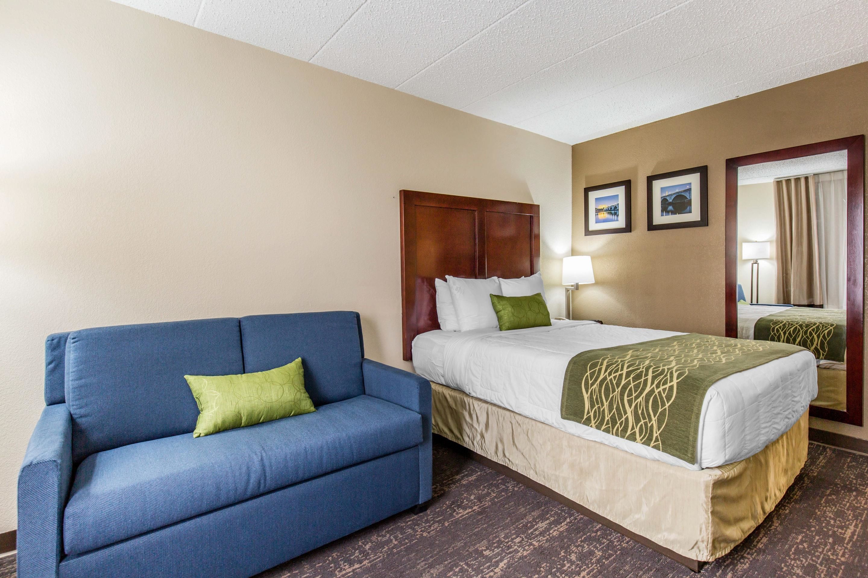 A hotel room with a bed, a blue sofa, and a wooden headboard.