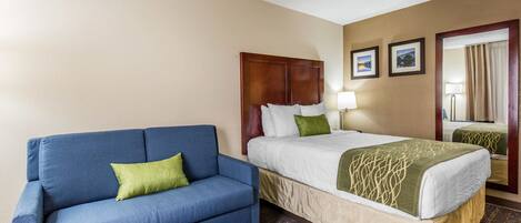 A hotel room with a bed, a blue sofa, and a wooden headboard.