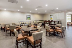 Une salle à manger d’hôtel avec de nombreuses tables et chaises, des tableaux encadrés aux murs et un sol carrelé.