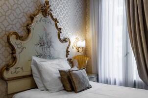 Un letto rifatto con cuscini bianchi e marroni, una testiera decorativa con motivi floreali e una lampada da comodino.