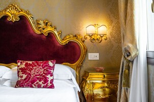 Un letto lussuoso con una testiera in velluto rosso, uno specchio con cornice dorata e un faretto a parete.