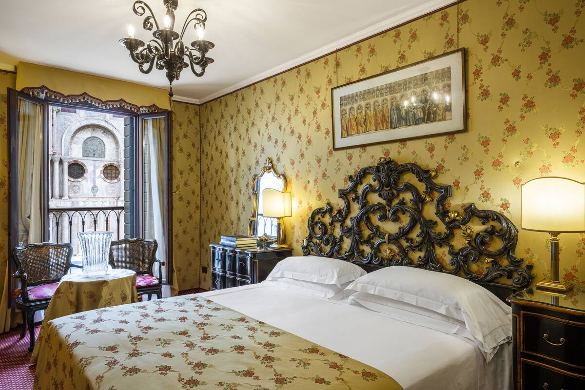 A hotel room with a bed, a chandelier, a mirror, a desk, and a chair.