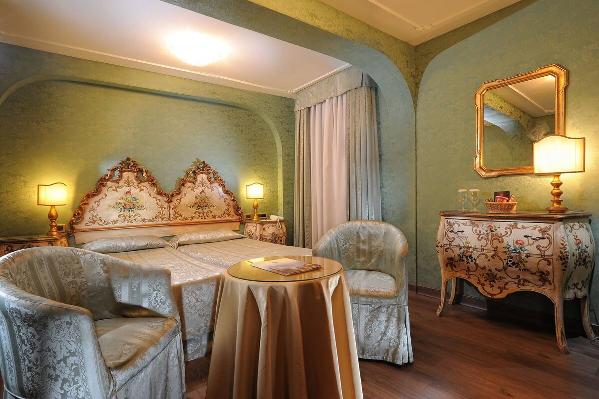 A room with a large bed, two armchairs, a small round table, a dresser, and a mirror.