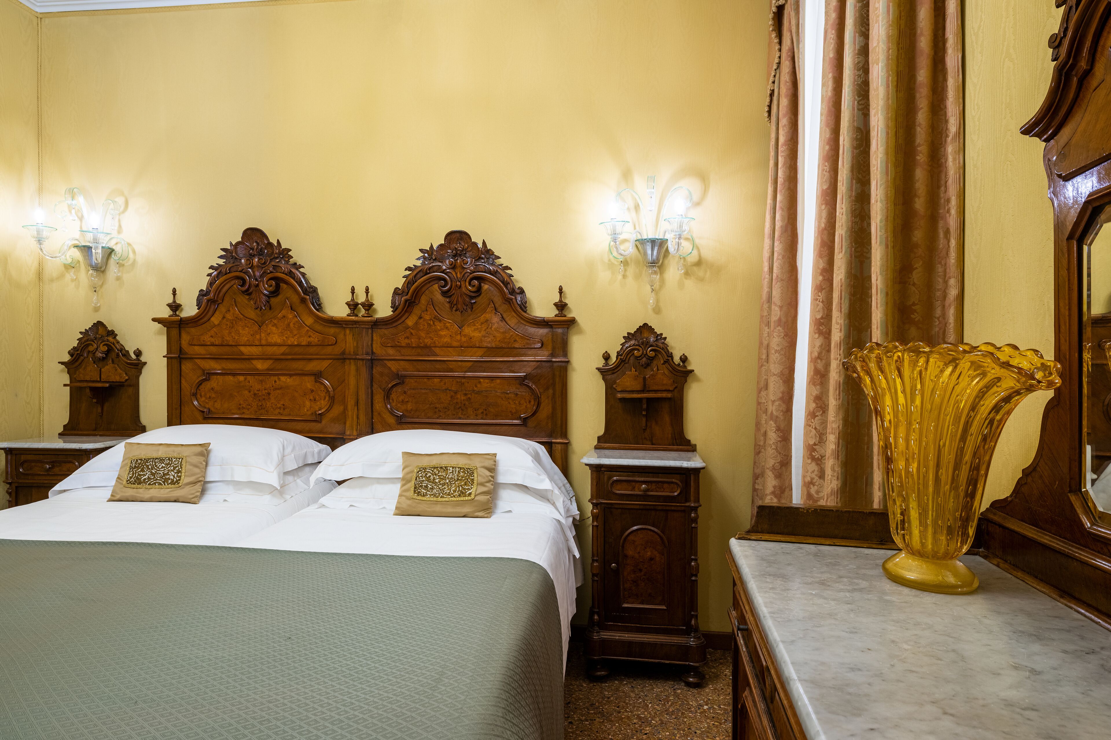A hotel room with a large bed, two nightstands, a mirror, and a decorative vase.