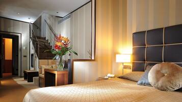 Een hotelkamer met een groot bed, een nachtkastje, een vaas met bloemen, een lamp en een trap.