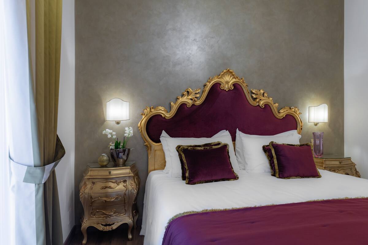 A bed with a gold and purple headboard, white bedding, and two bedside tables with lamps.