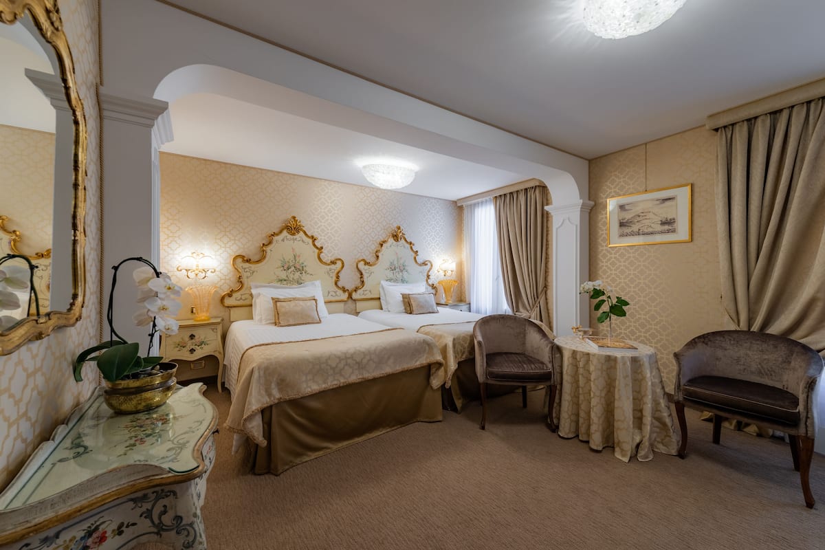 A hotel room with two beds, a sitting area, a small table, and a decorative mirror.