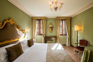 Una camera d'hotel con un letto grande, una sedia di legno, un tavolino e un lampadario.