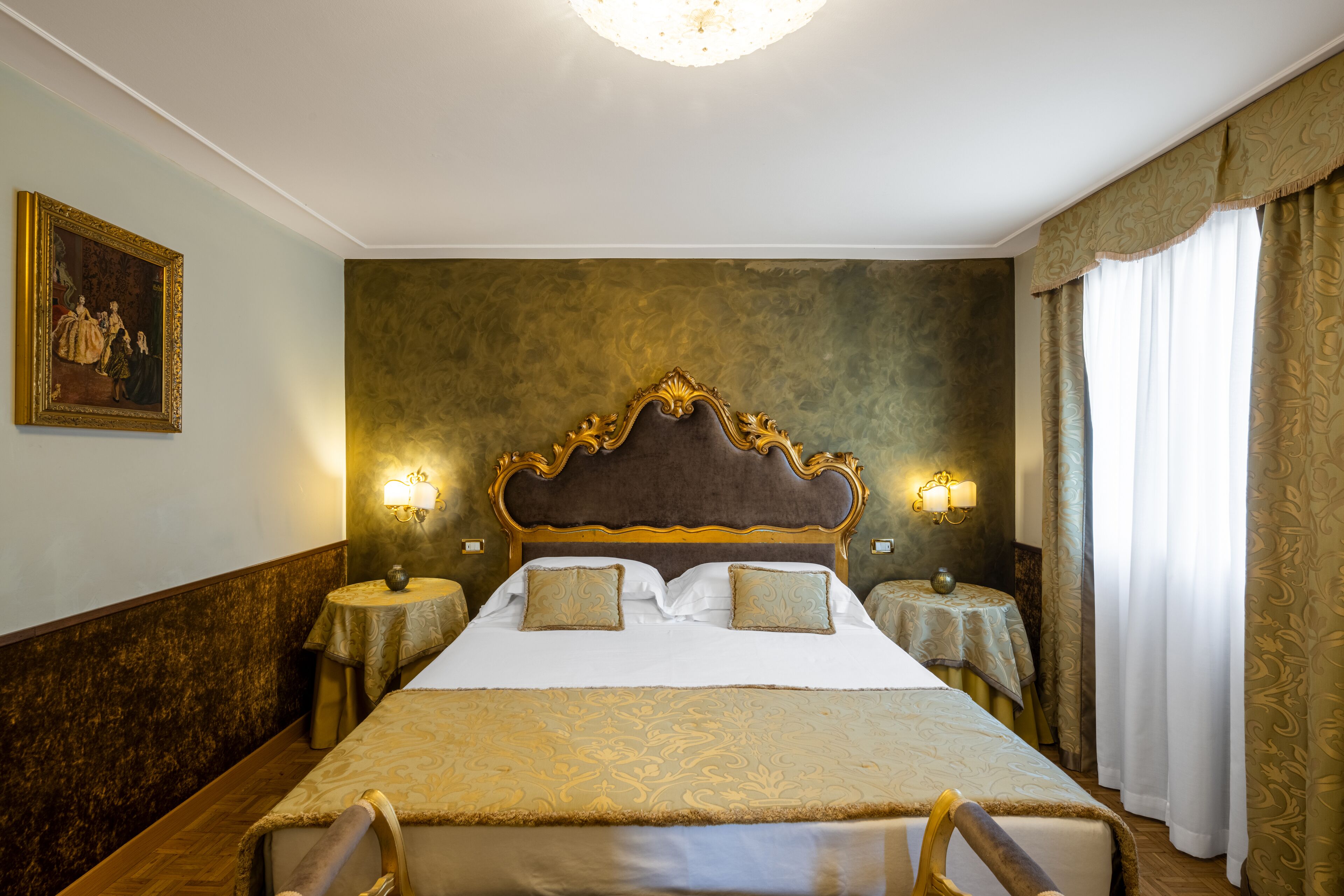 A large bed with a wooden headboard, two bedside tables with lamps, and a painting on the wall.