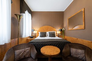 Una habitación de hotel con una cama grande, dos lámparas de noche, una mesa redonda y dos sillones.