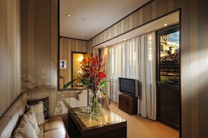 Una sala moderna con un sofá, una mesa de centro con un jarrón de flores, un televisor y vistas a un edificio tradicional a través de una ventana.