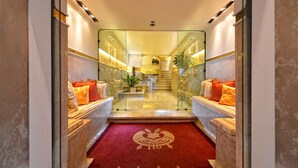 Un vestíbulo de hotel con piso de mármol, una alfombra roja con un logotipo y una escalera que sube al segundo piso.