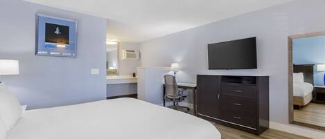 Habitación de hotel con cama, escritorio, silla, televisor y espejo.