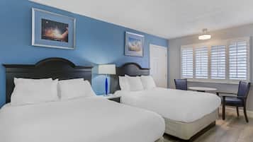 Habitación de hotel con dos camas, una mesita, una silla y una ventana con persianas.
