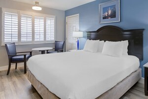 A hotel room with a large bed, a desk with a chair, a round table, and a picture on the wall.