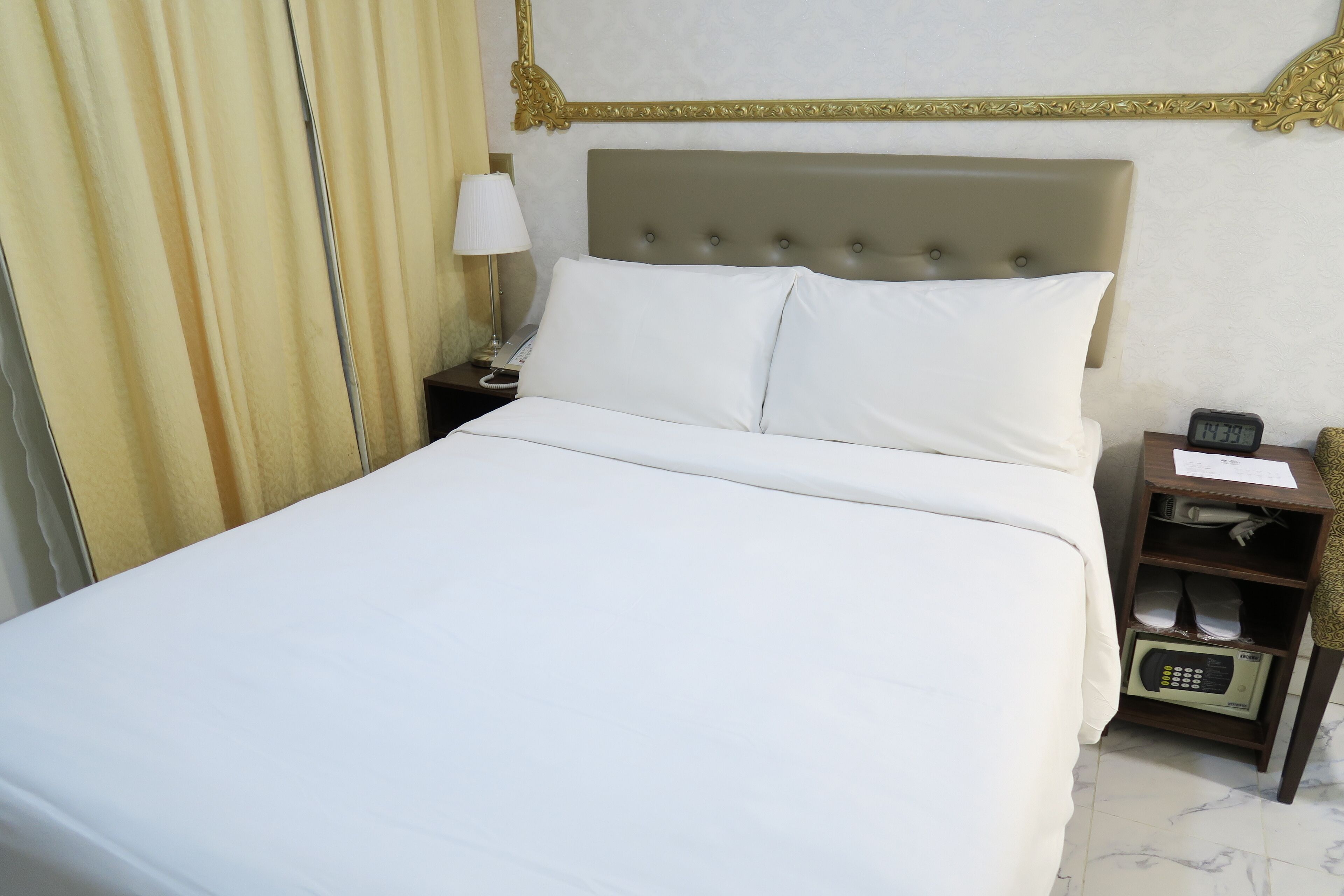 A neatly made bed with white linens, a bedside table with a lamp, and a digital clock displaying 7:39.