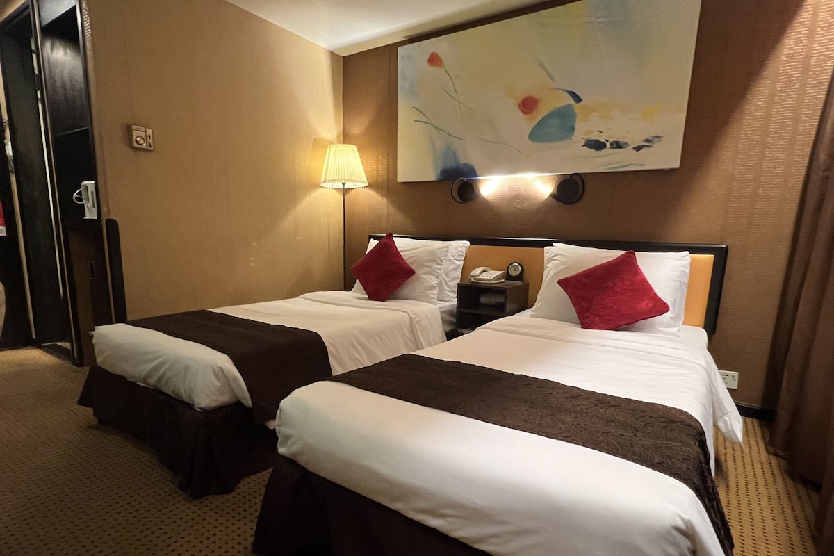 Une chambre d’hôtel avec deux lits, une table de chevet, une lampe et un tableau au mur.