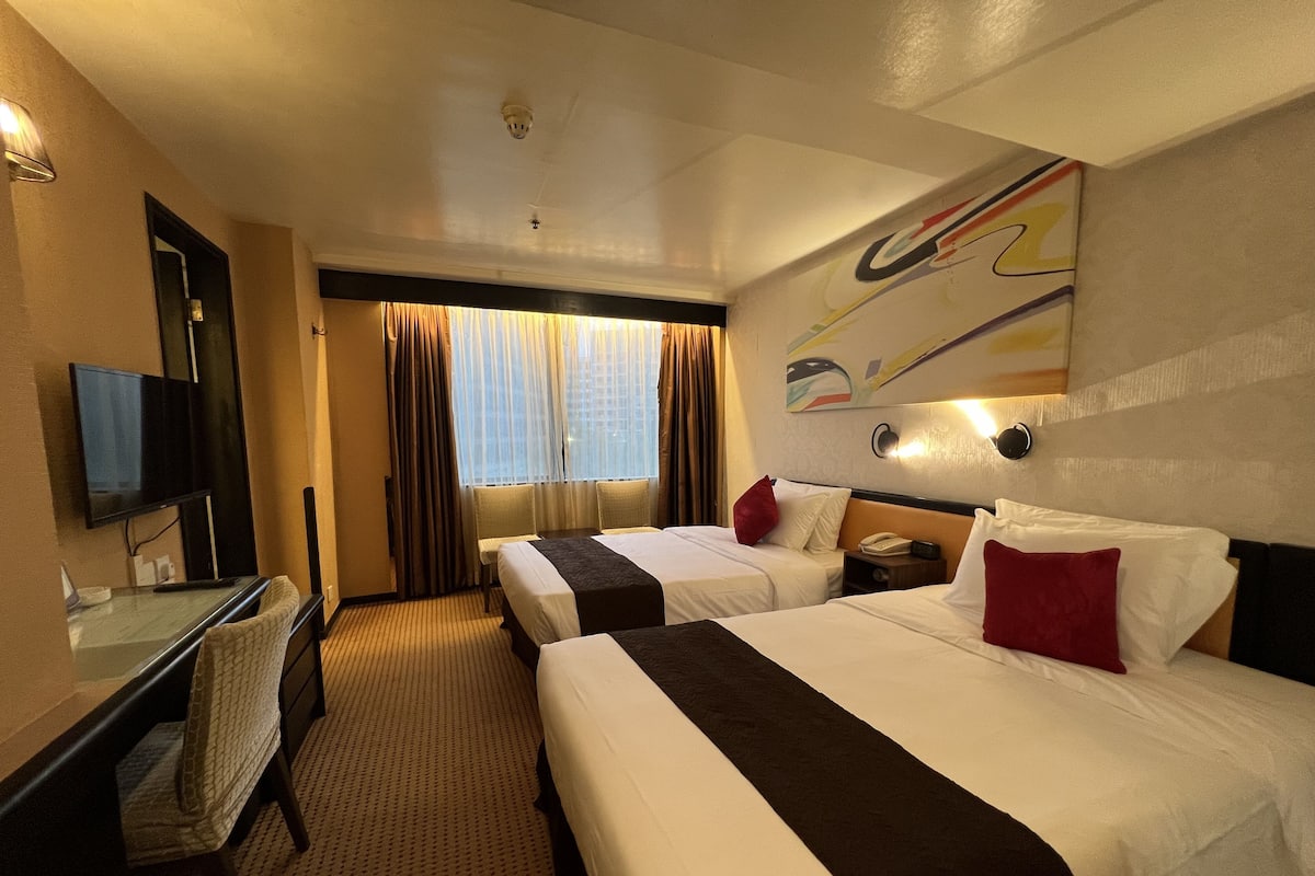 Une chambre d’hôtel avec deux lits, un bureau, une chaise, une télévision et une fenêtre avec des rideaux.