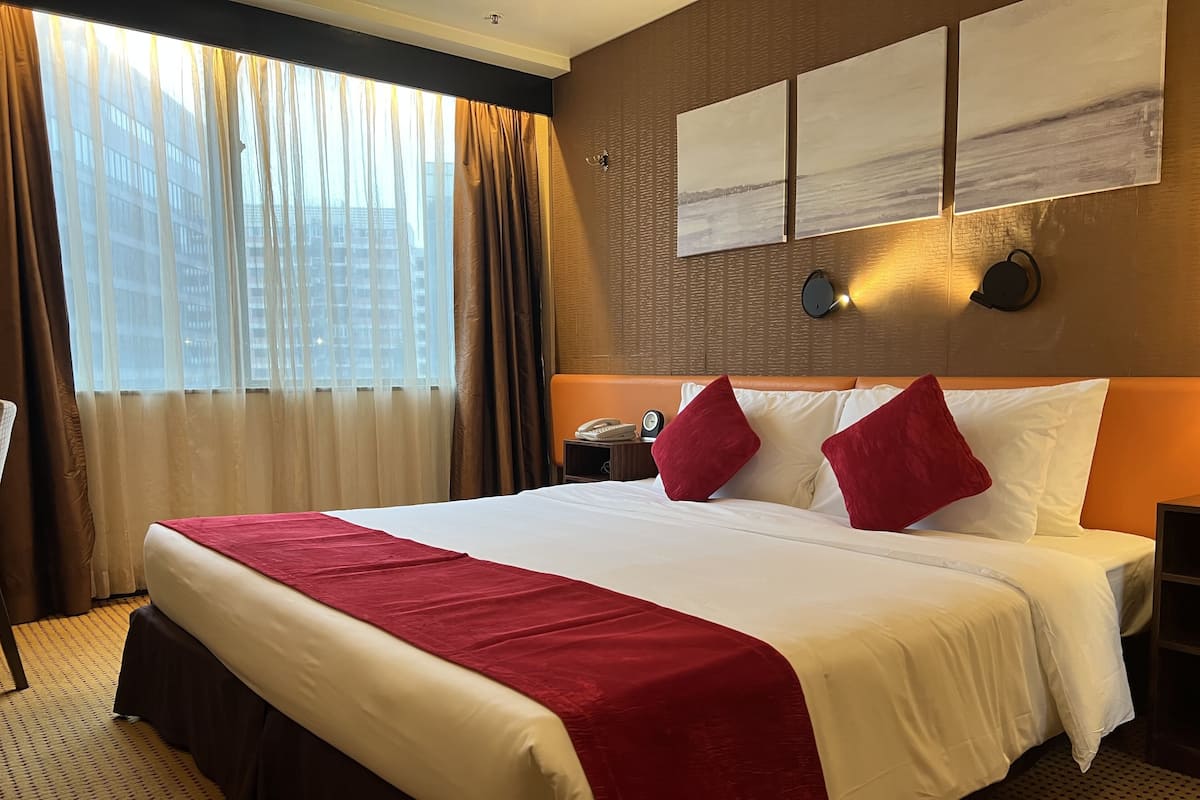 Une chambre d’hôtel avec un grand lit, une table de chevet, un téléphone et une vue sur les bâtiments par la fenêtre.