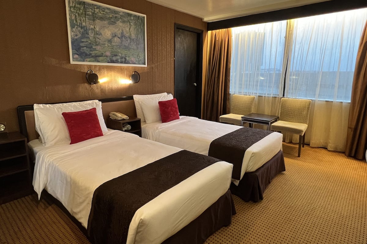 Une chambre d’hôtel avec deux lits, un tableau au mur, un bureau et une fenêtre avec des rideaux.