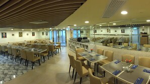 A hotel dining area with multiple tables and chairs, a kitchen area, and a mirrored wall. - Best Western Plus Tsim Sha Tsui (Kowloon)