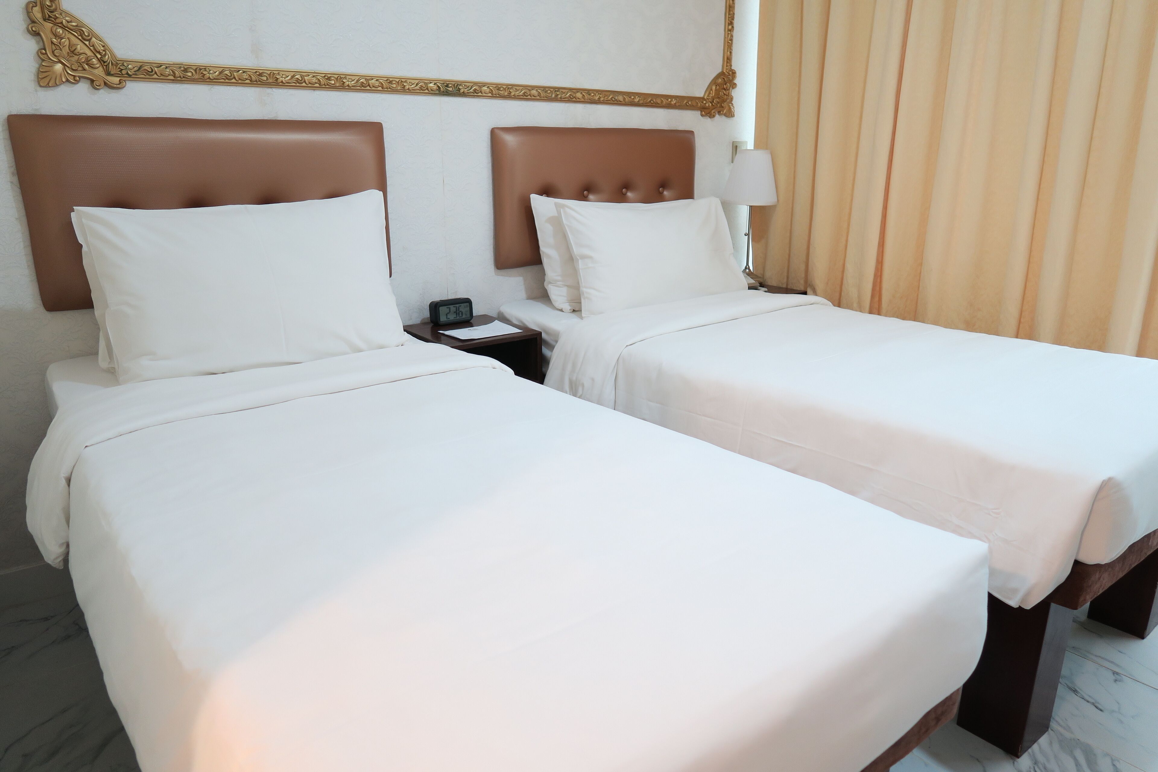 Two single beds with headboards, a nightstand with a clock, and a window with curtains.
