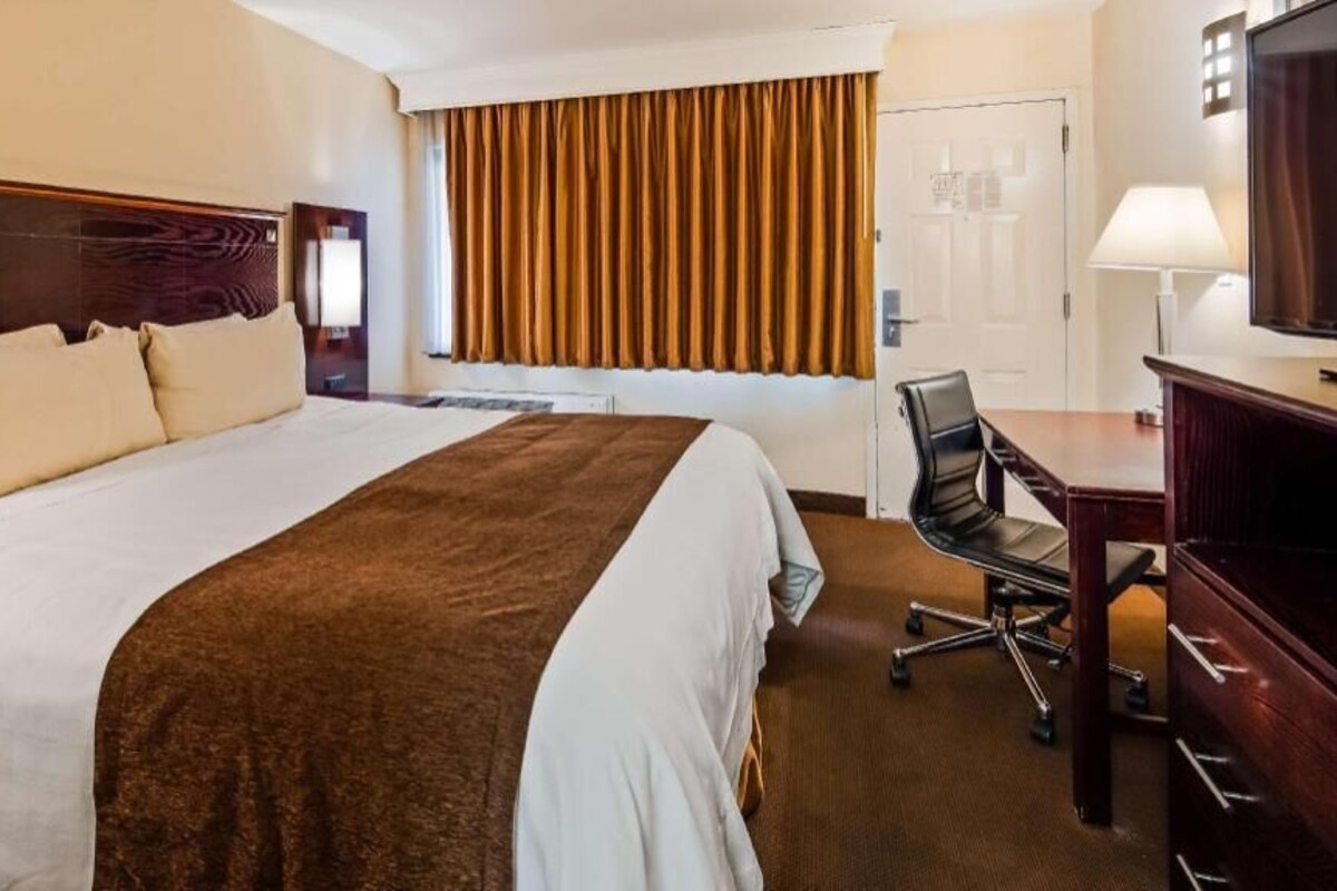 A hotel room with a large bed, a desk, a chair, a television, and a window with curtains.
