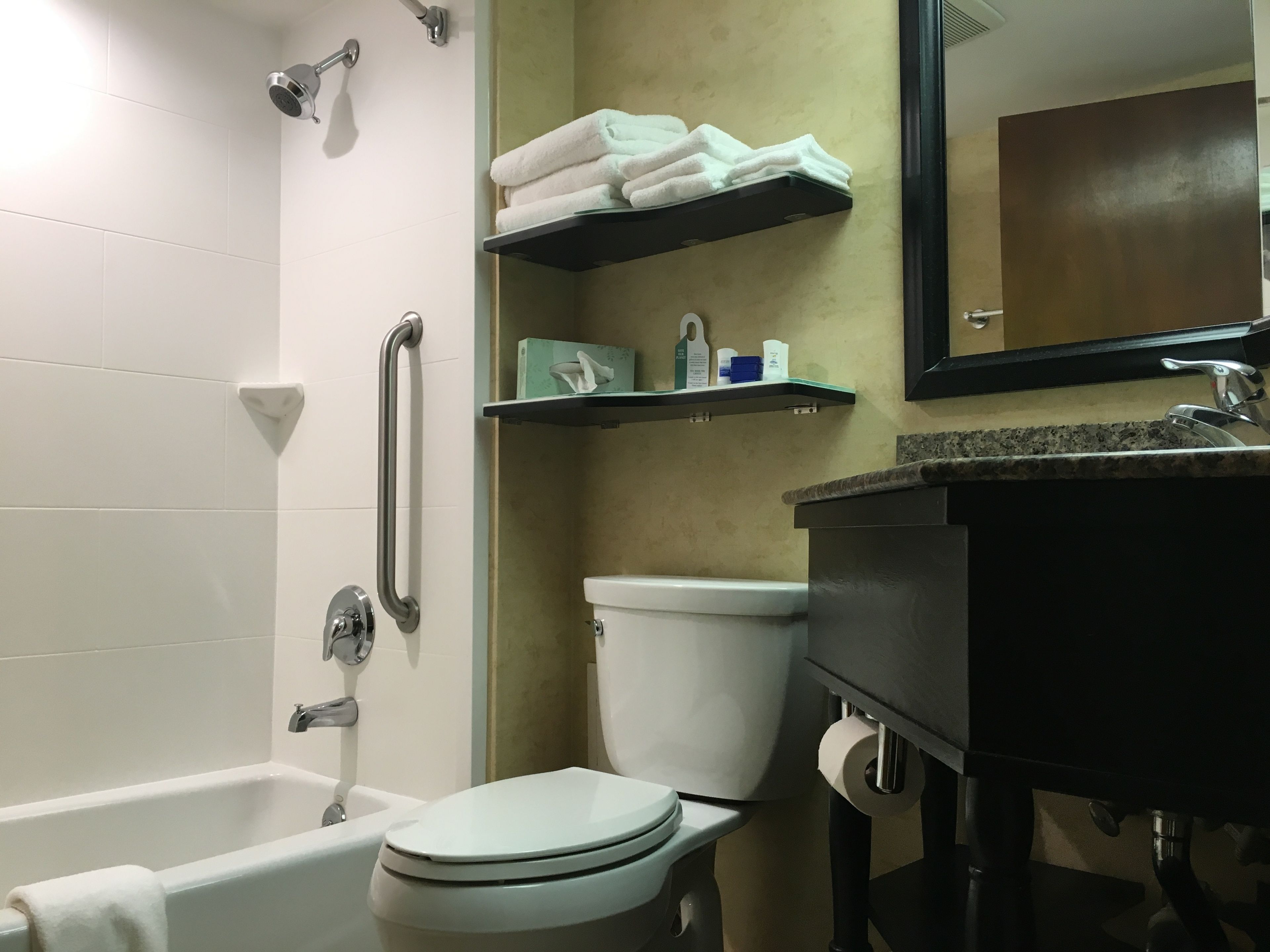 A bathroom with a bathtub, toilet, and sink. There are shelves with towels and toiletries.