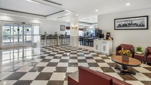 A hotel lobby with a checkered floor, seating area, bar, and a framed cityscape picture on the wall. - Best Western Bar Harbour Inn (Massapequa Park)