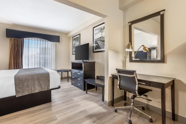 Habitación de hotel con cama, escritorio, silla, televisor y un espejo grande.