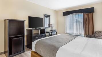 Hotelkamer met een groot bed, een bureau met een flatscreen televisie, een kleine koelkast en een raam met gordijnen.