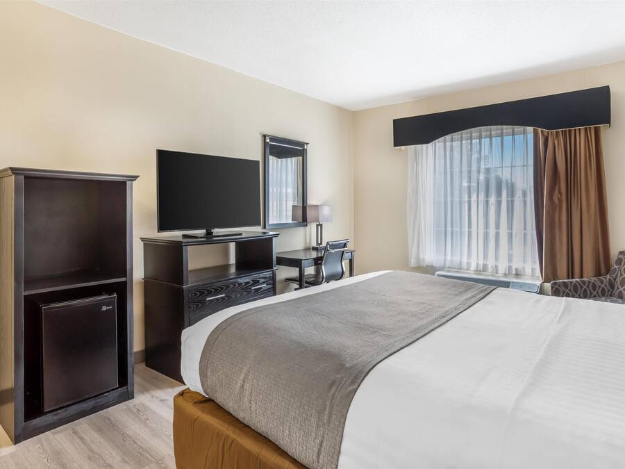 Hotelkamer met een groot bed, een bureau met een flatscreen televisie, een kleine koelkast en een raam met gordijnen.