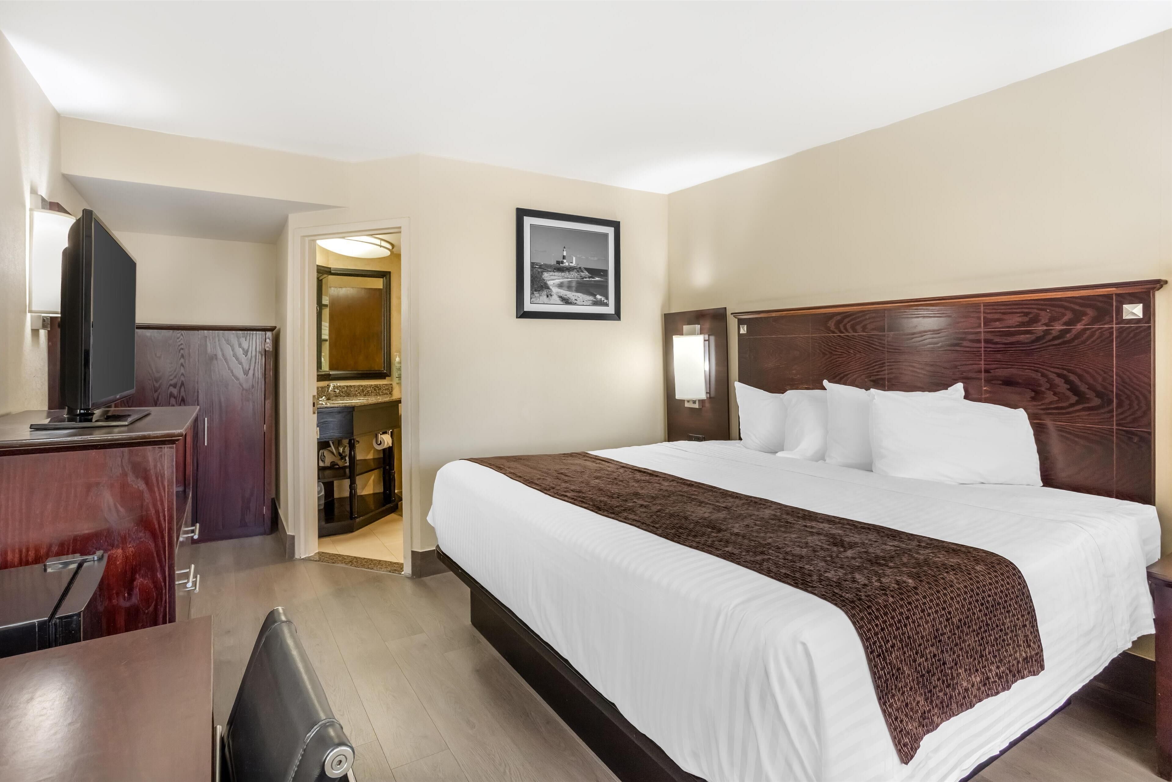 Une chambre d’hôtel avec un grand lit, un bureau, une télévision et un tableau encadré au mur.