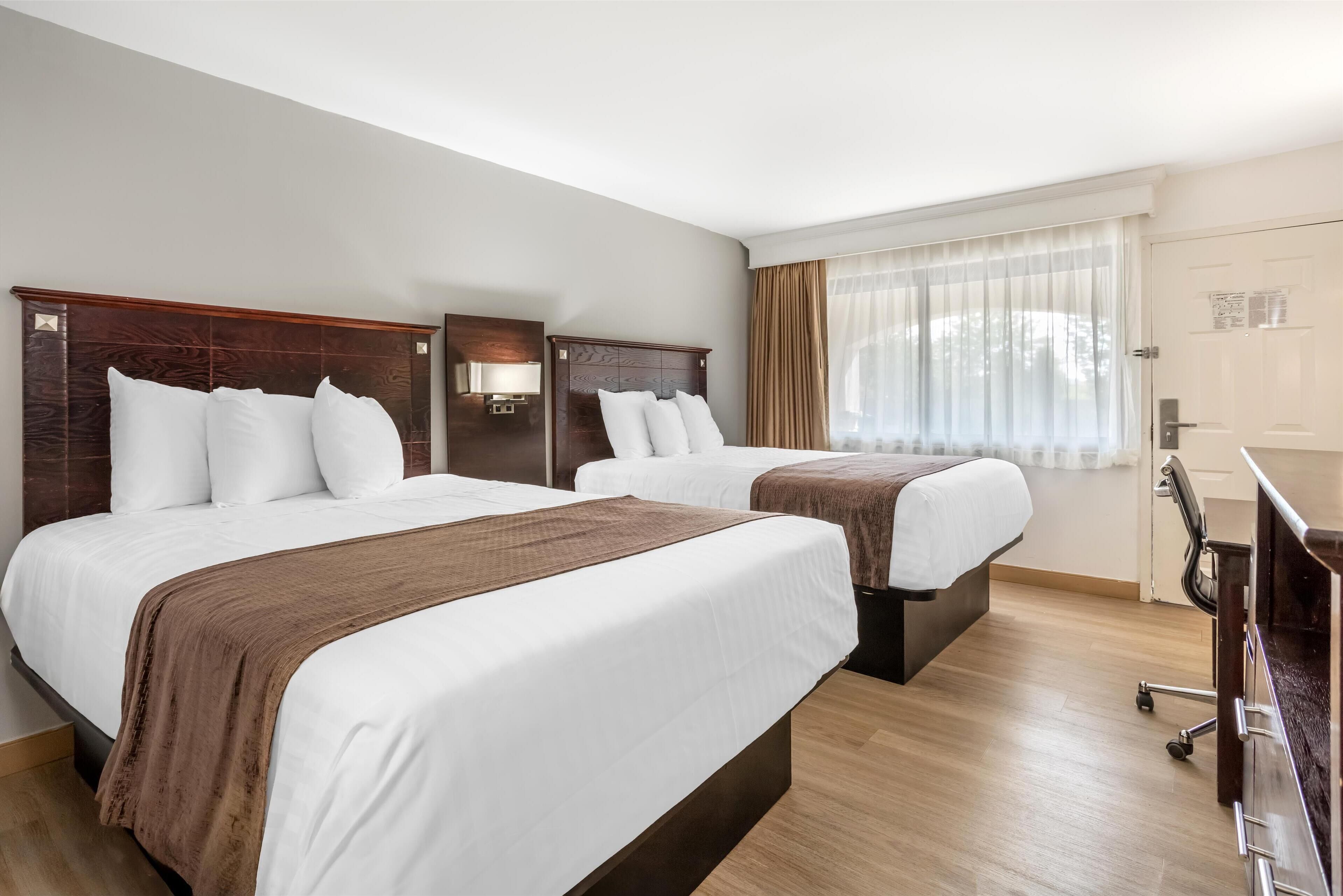 Habitación de hotel con dos camas, un escritorio y una ventana con cortinas.