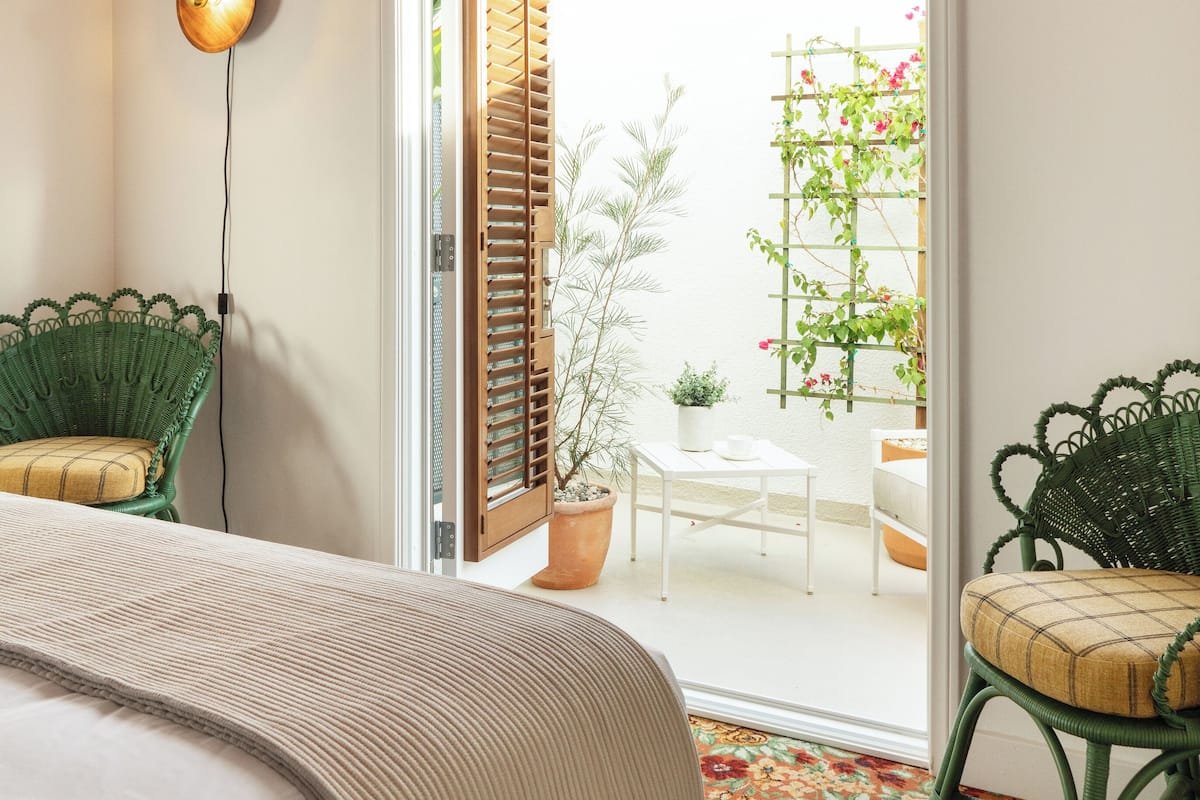 Een slaapkamer met een bed, een groene stoel, een witte tafel en een plant in een pot.