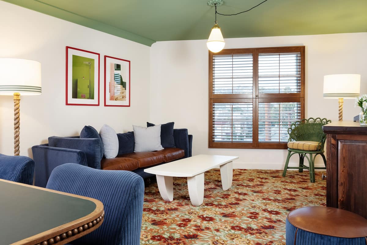 Een woonkamer met een bruine leren bank, blauwe fauteuils, een witte salontafel en een kamerbreed tapijt met een patroon.