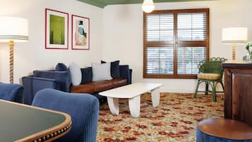 Una sala de estar con un sofá de cuero marrón, sillones azules, una mesa de centro blanca y una alfombra estampada.