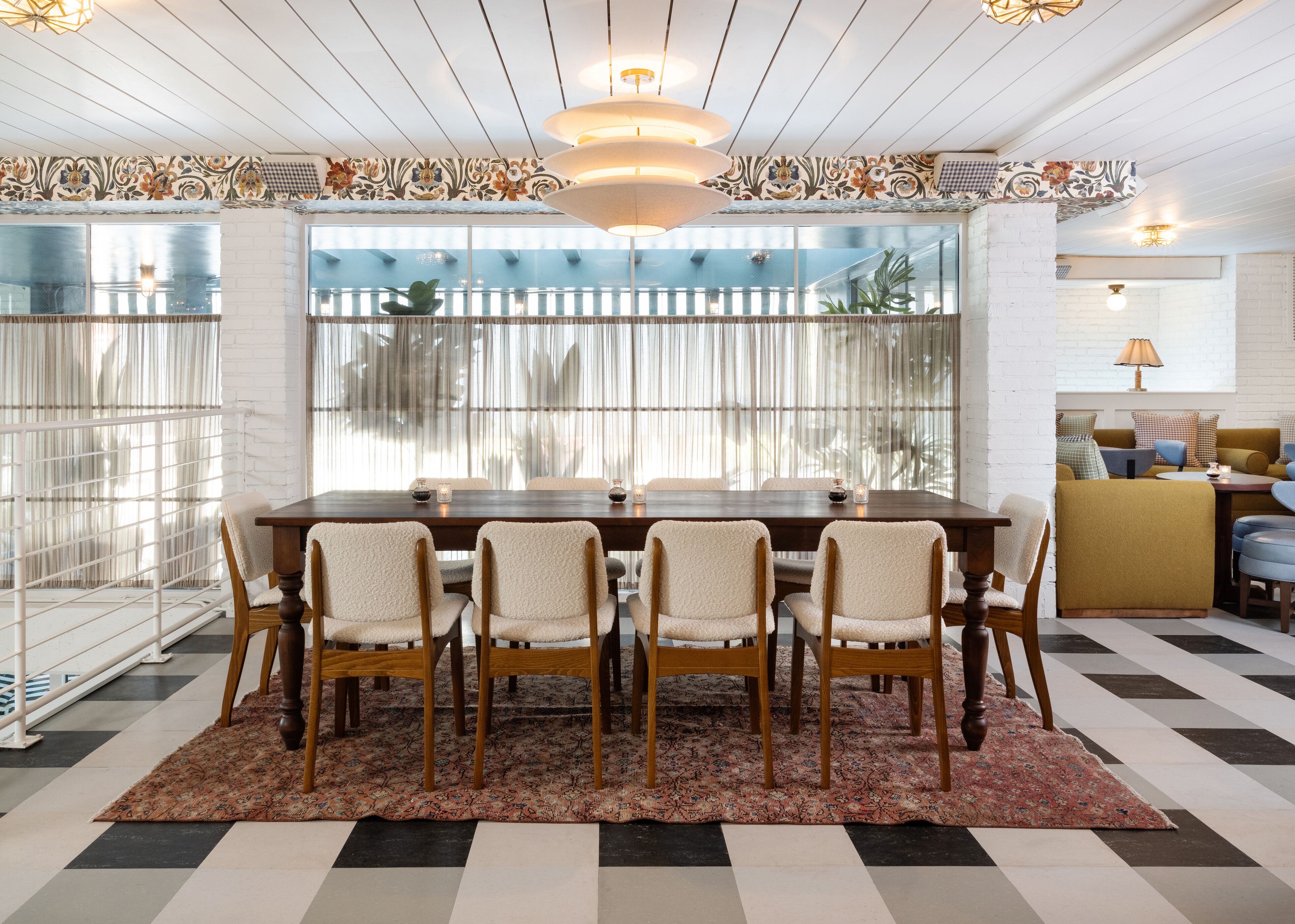 Un coin repas avec une table et des chaises en bois, un tapis à motifs et une vue dégagée grâce à de grandes fenêtres.