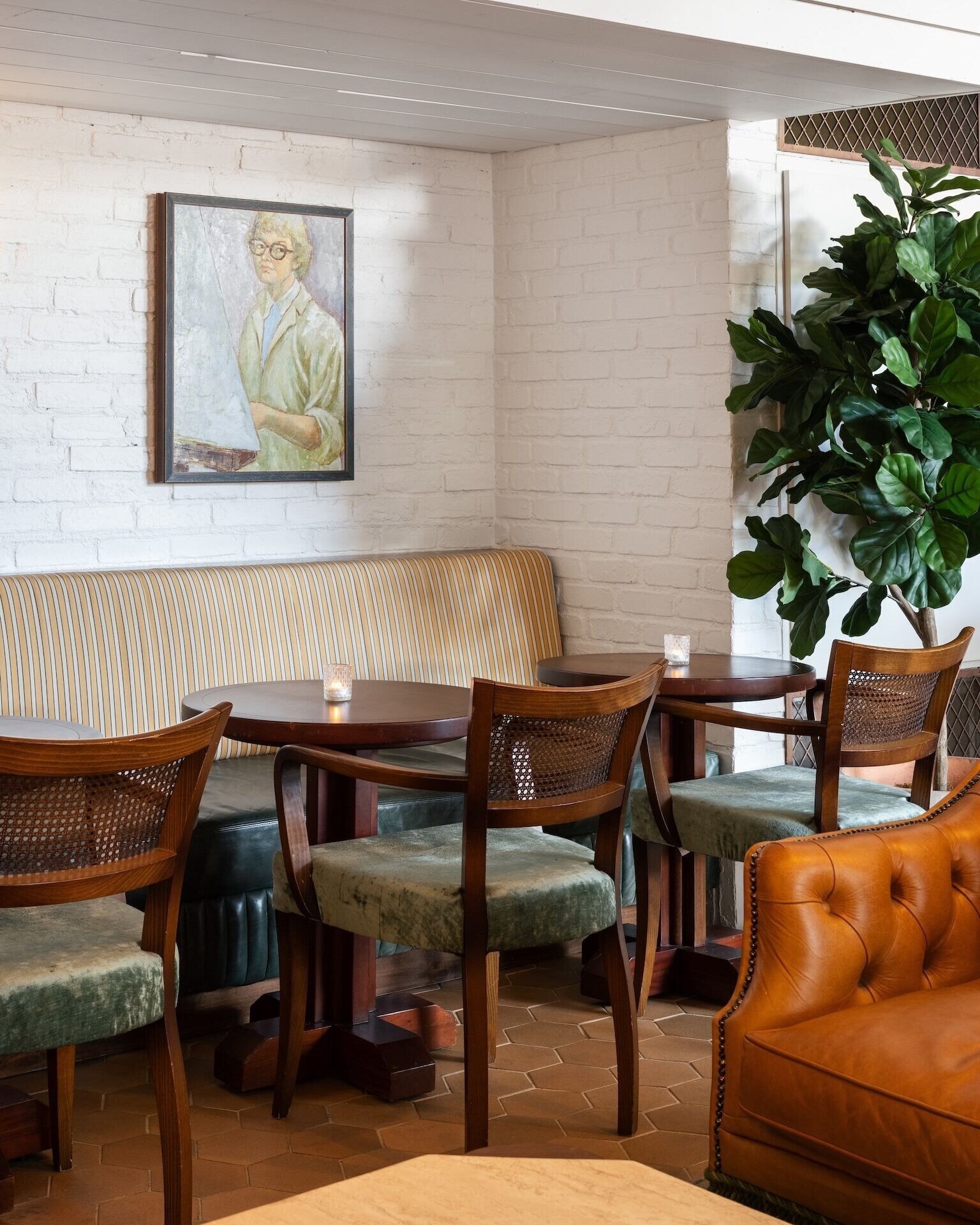 A dining area with a brick wall, a painting, a large plant, and a leather couch.