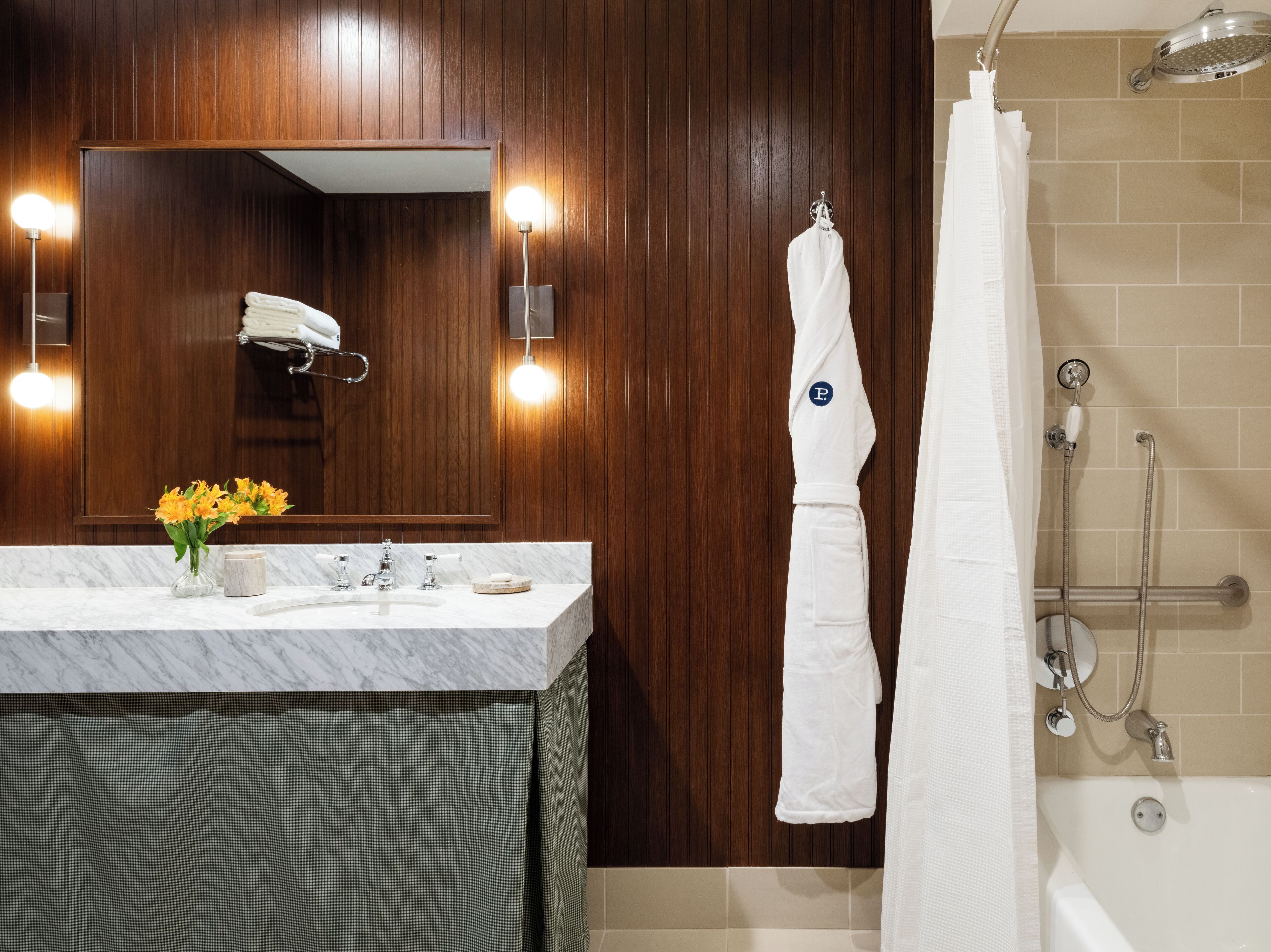 Un baño con lavamanos de mármol, paneles de madera en las paredes, un espejo con luces, un perchero y una zona de ducha.