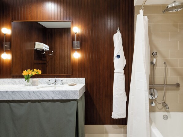 Une salle de bain avec un lavabo en marbre, des murs recouverts de panneaux en bois, un miroir avec éclairage intégré, un porte-serviettes et un espace douche.