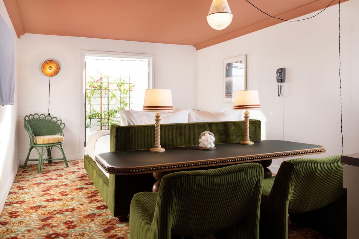 Een kamer met een groen bekleden bankstel, een kleine tafel met twee lampen, een kamerbreed tapijt en een raam met uitzicht op groen.