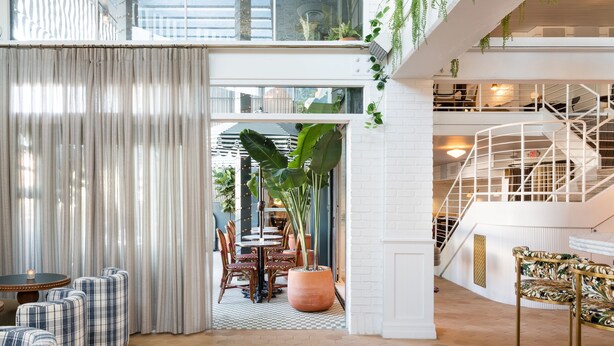 A spacious indoor area with a high ceiling, a staircase, and a dining area with chairs and tables.