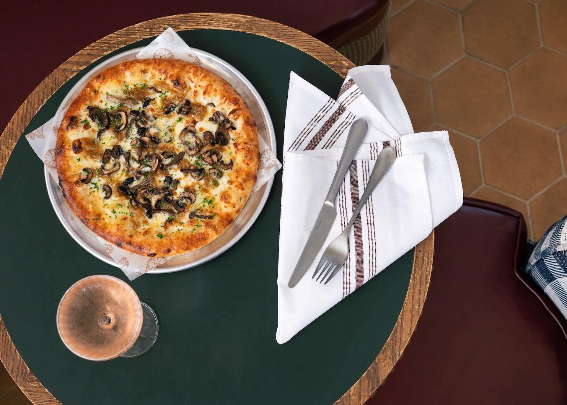 A pizza on a round table with a napkin and cutlery beside it.