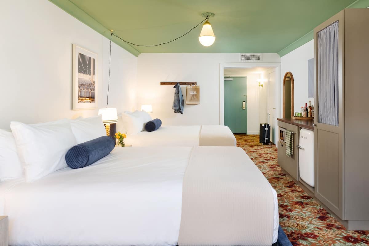 Een hotelkamer met twee bedden, een kaptafel, een spiegel en een deur naar een badkamer.